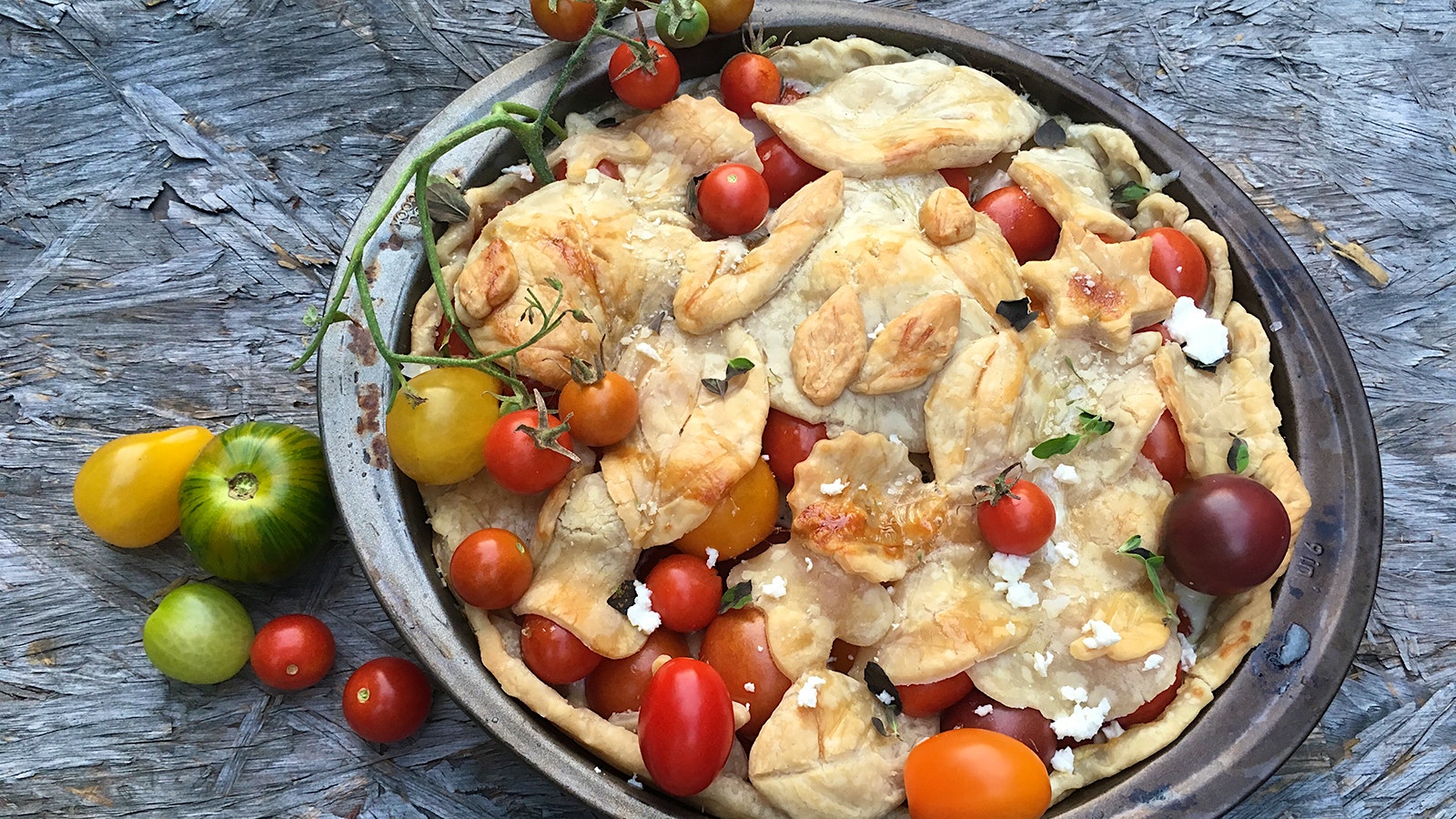 Tomato pie with leaf-shaped patterns in the crust and small tomatoes on top, next to a glass of white wine
